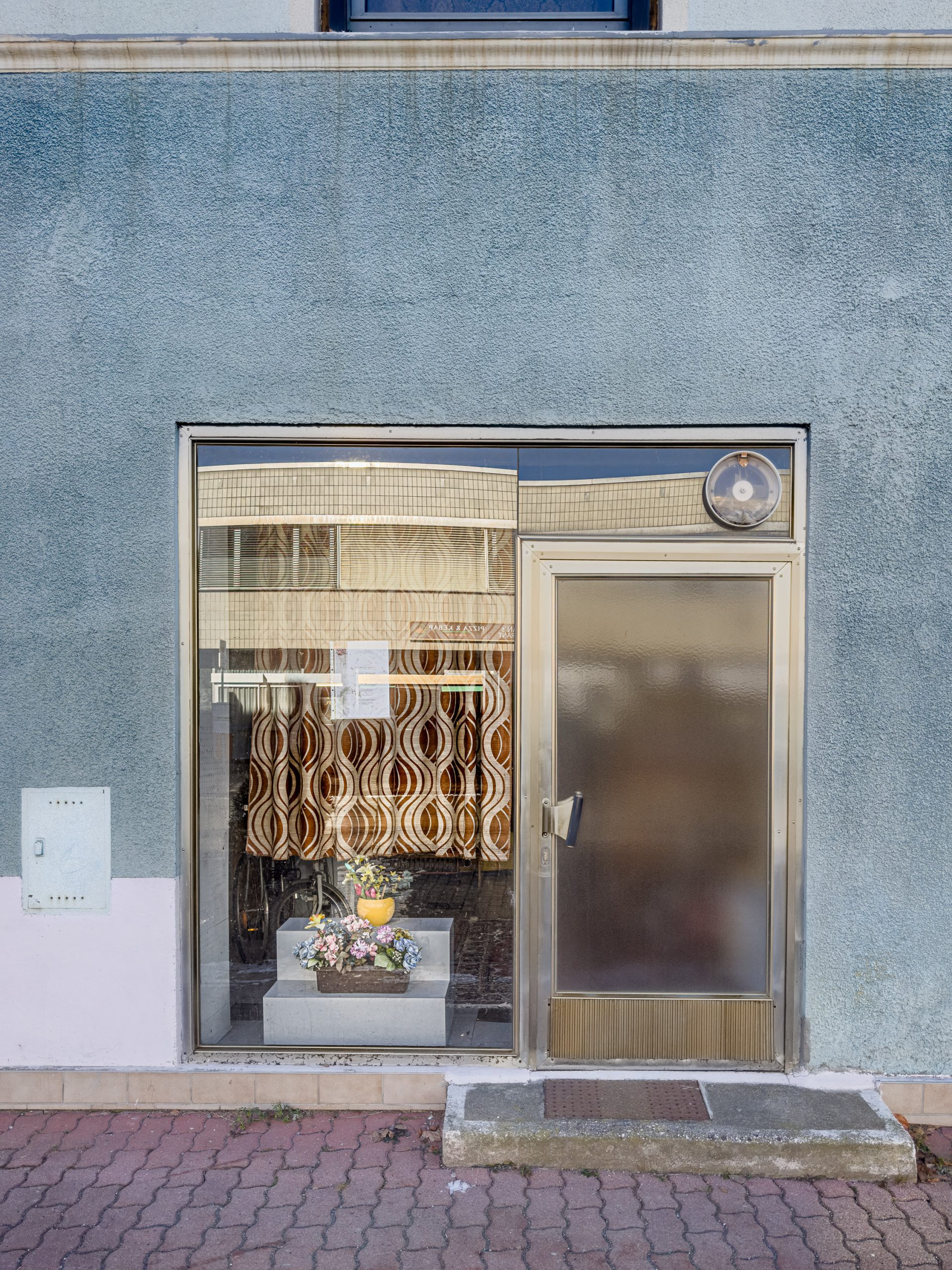 Former storefront entrance in Zeltweg, Austria, showing a closed door, window display, and faded facade.